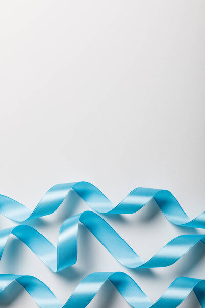 top view of blue wavy satin ribbons on grey background with copy space