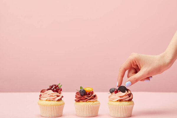 cropped view of woman with sweet cupcakes with fruits and berries isolated on pink