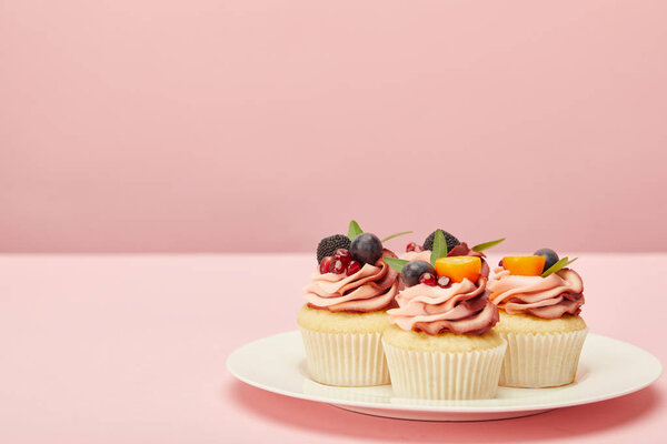 sweet cupcakes with berries and fruits on plate on pink surface