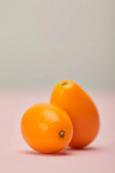 灰色粉红色表面上的两个成熟的金桔 — 图库照片