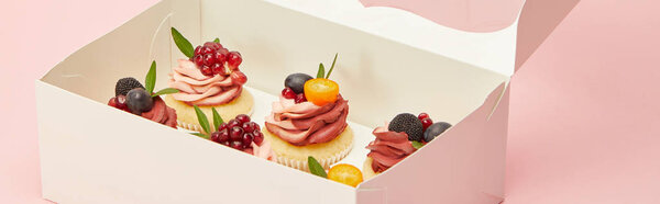 панорамный снимок кексов с ягодами и фруктами в картонной коробке, изолированной на розовый
