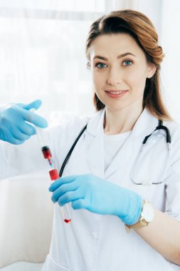 kan örneği ve test tüpü ile şırınga tutan lateks eldiven gülümseyen doktor 