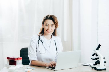 klinikte dizüstü bilgisayar kullanarak stetoskop ile beyaz ceketli doktor