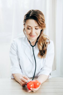 klinikte stetoskop dinleme plastik kalp ile gülümseyen doktor