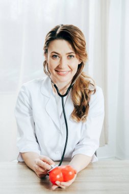 klinikte stetoskop dinleme plastik kalp ile gülümseyen doktor