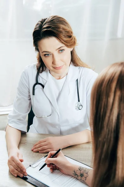 cropped view of donor signing registration form and doctor in white coat