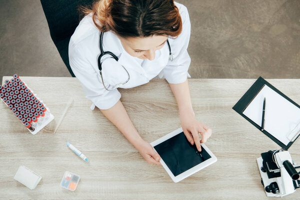 overhead view of doctor in white coat using digital tablet with blank screen