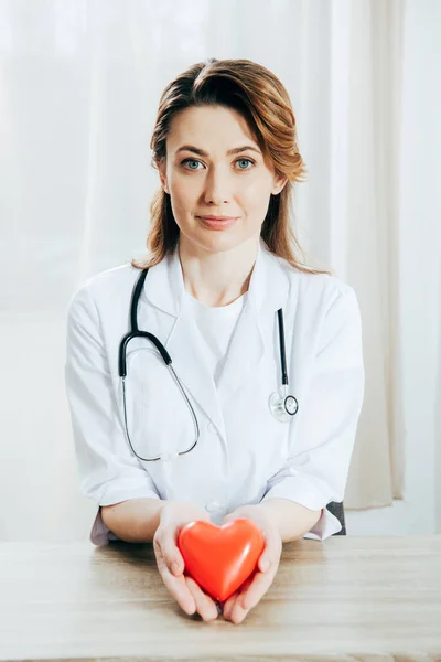 Uśmiechnięty Lekarz Białym Płaszczu Stetoskop Trzymając Plastikowe Serce — Zdjęcie stockowe
