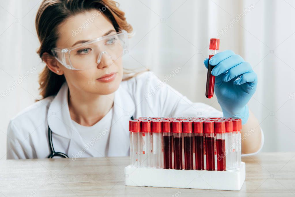 concentrated doctor in protective goggles holding test tube with blood