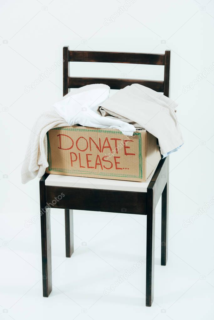cardboard box with donated clothes on wooden chair on white