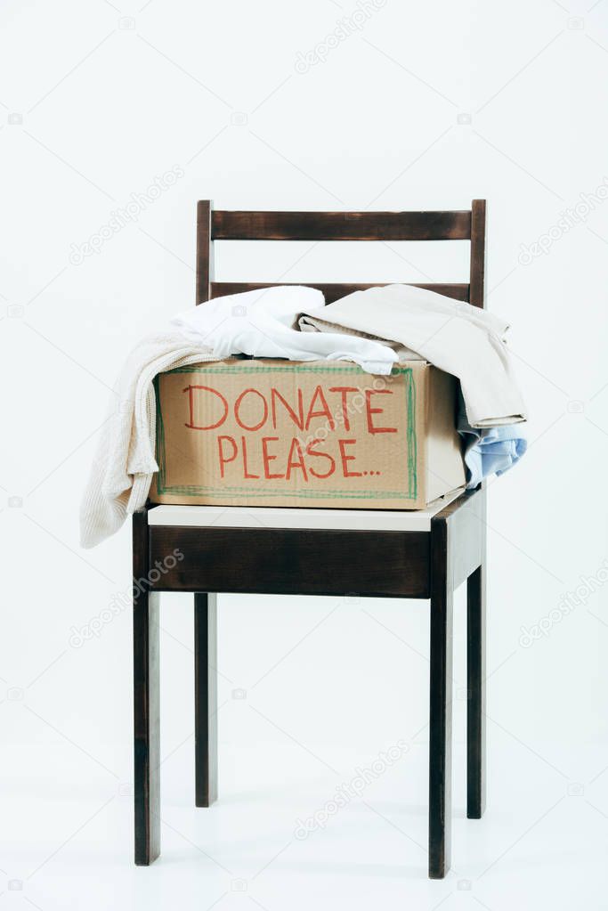 cardboard box with donated clothes on wooden chair on white