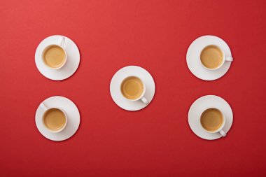 top view of white cups with coffee on saucers on red background clipart