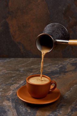 pouring coffee from cezve into brown cup on marble surface clipart