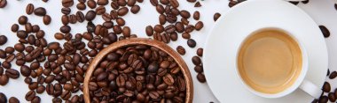 top view of coffee in cup on saucer near scattered roasted beans and wooden bowl, panoramic shot clipart