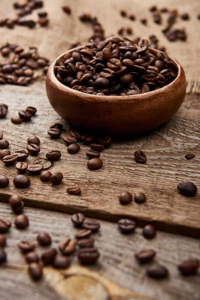 新鲜烤咖啡豆的选择性焦点散落在木板上的碗附近 — 图库照片
