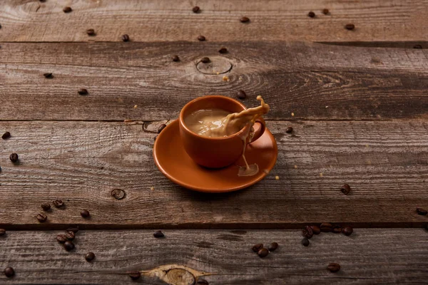 Koffie Splash Bruine Beker Houten Tafel Met Verspreide Koffiebonen — Stockfoto