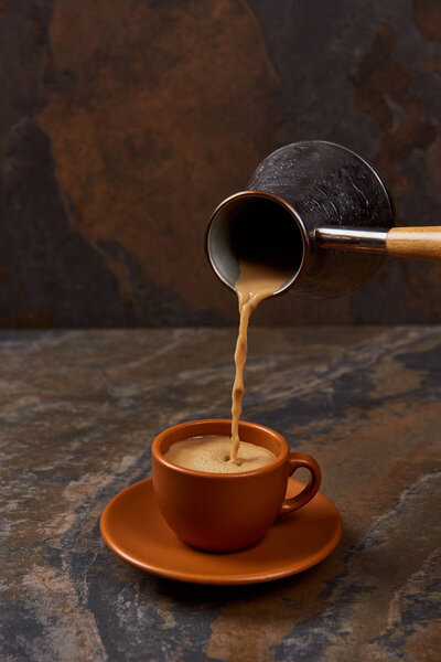 pouring coffee from cezve into cup on saucer on marble surface