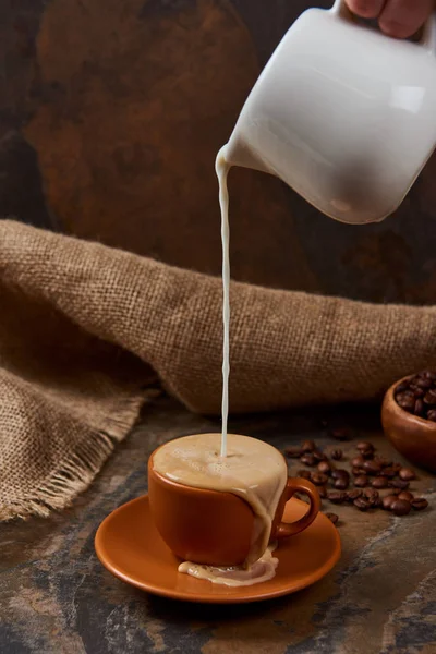 大理石のテーブルの上にコーヒーとカップにミルクを注ぐ人のトリミングされたビュー — ストック写真