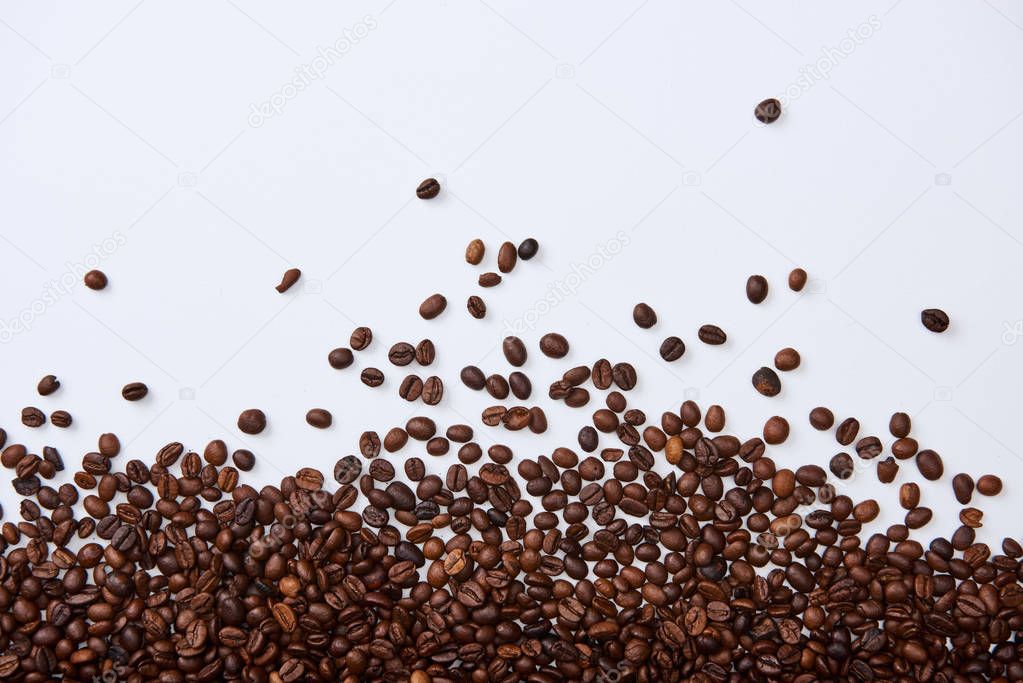 top view of scattered brown roasted beans on white background