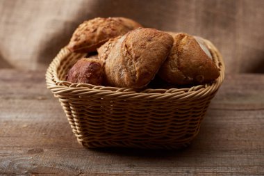 fresh baked buns in wicker basket on wooden table with sackcloth on background clipart