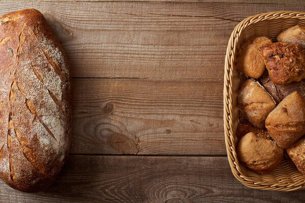 верхний вид плетеной корзины с булочками и буханкой хлеба на деревянном столе
