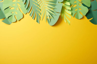 top view of paper cut green palm leaves on yellow background with copy space clipart
