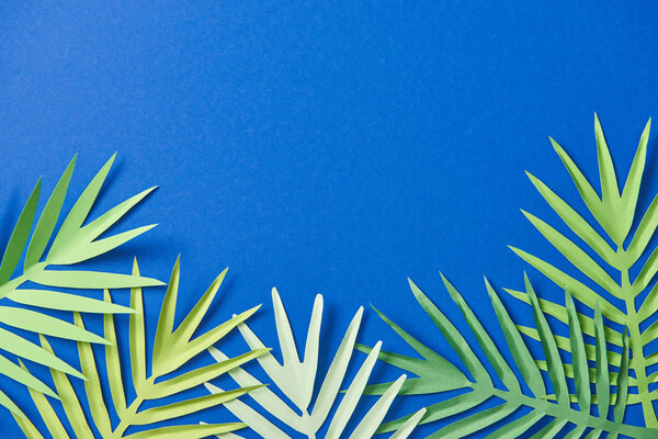 top view of paper cut exotic leaves on blue background with copy space