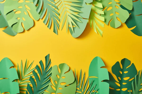 top view of paper cut green palm leaves on yellow background with copy space