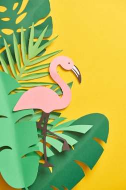 kağıt kesme yeşil palmiye yaprakları ve sarı arka plan üzerinde sevimli pembe flamingo üst görünümü