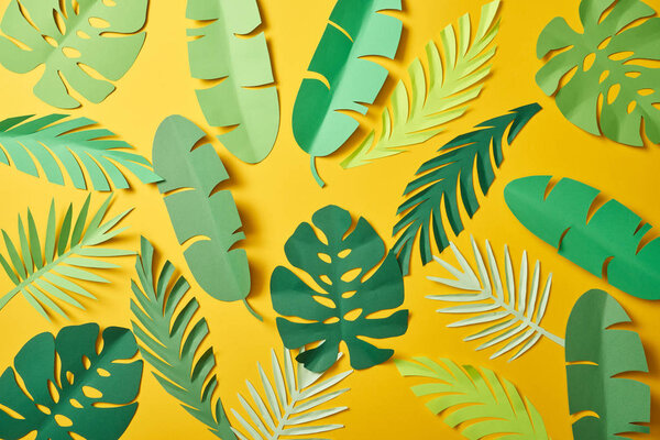 top view of paper cut green palm leaves on yellow background, seamless pattern