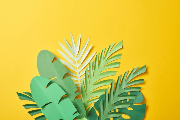 bunch of paper cut exotic green palm leaves on yellow background with copy space