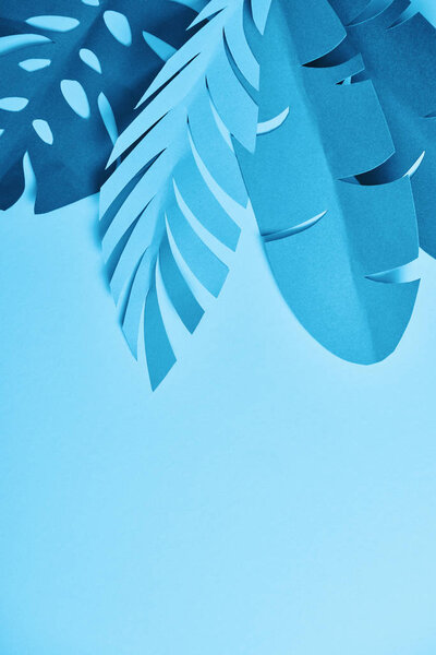 top view of blue paper cut palm leaves on blue background with copy space
