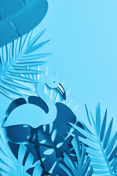 top view of blue minimalistic paper cut palm leaves and flamingo on blue background with copy space