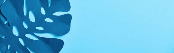 top view of blue exotic paper cut palm leaves on blue background with copy space, panoramic shot