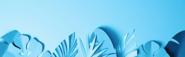 top view of blue exotic paper cut palm leaves on blue background with copy space, panoramic shot