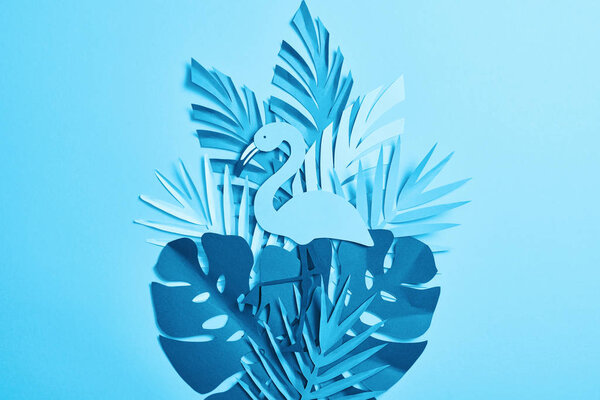 top view of blue exotic paper cut flamingo on palm leaves on blue background with copy space