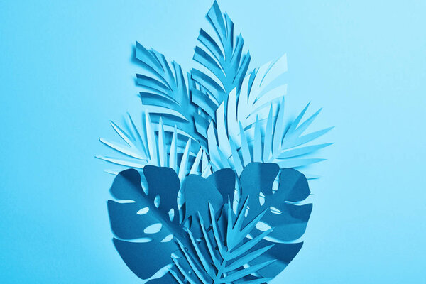 top view of blue exotic paper cut palm leaves on blue background with copy space