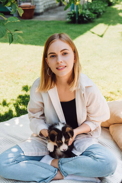 happy blonde girl sitting on blanket in garden with adorable puppy at sunny day