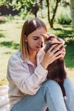 yeşil bahçede sevimli köpek yavrusu tutan kapalı gözlü sarışın kız