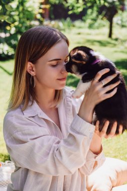 yeşil bahçede sevimli köpek yavrusu tutan kapalı gözleri ile gülümseyen sarışın kız