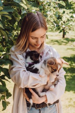 blonde girl holding cute puppies in garden near green tree  clipart