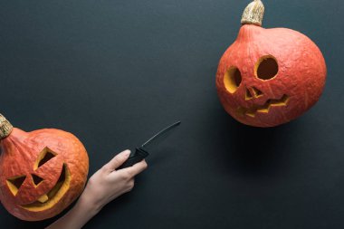 siyah arka plan üzerinde oyulmuş ürkütücü Halloween kabaklar yakınında bıçak tutan kadın kısmi görünümü
