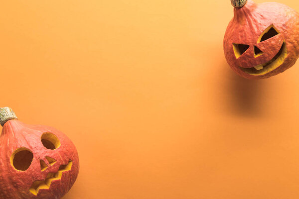 top view of carved spooky Halloween pumpkins on orange background with copy space