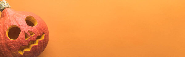 top view of spooky carved Halloween pumpkin on orange background, panoramic shot