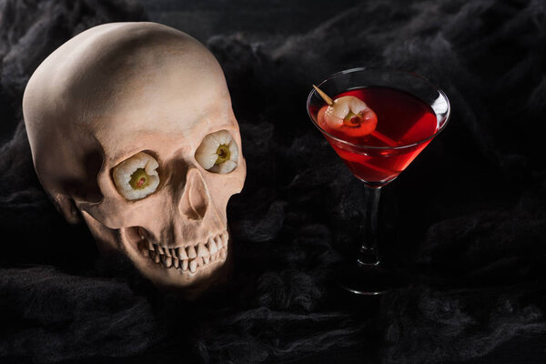 red cocktail near spooky skull on black background