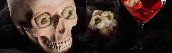 panoramic shot of red cocktail near skull on black background