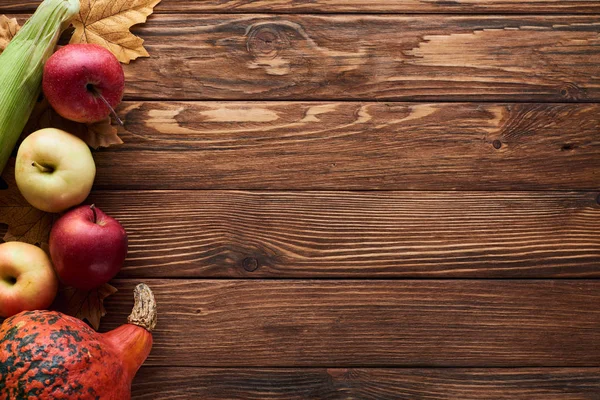 玉米和苹果在棕色木表面上与干燥的秋叶的顶视图 — 图库照片