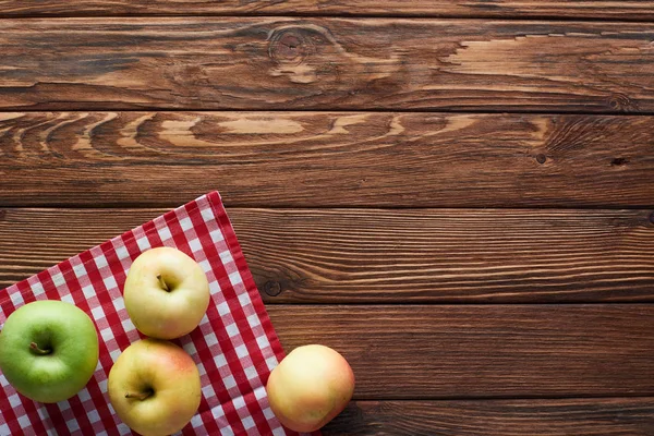 コピースペース付きの木製の表面に熟したリンゴとチェッカーテーブルクロスのトップビュー — ストック写真