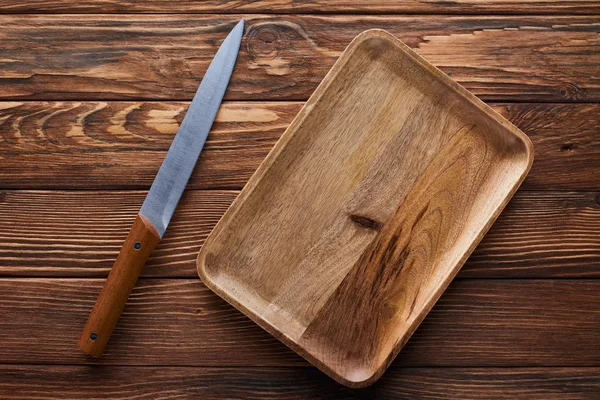 茶色の木製の表面にナイフの近くに空の長方形の皿の上の眺め — ストック写真