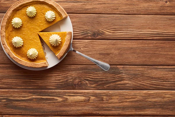 茶色の木製のテーブルの上にへらとプレート上にホイップクリームとおいしいカボチャのパイ — ストック写真